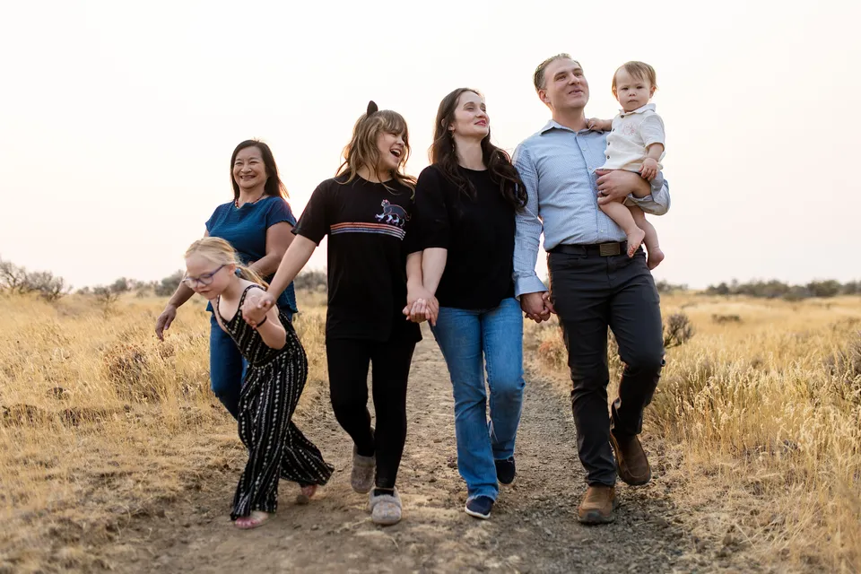 Family holding hands and walking along a sunlit field path