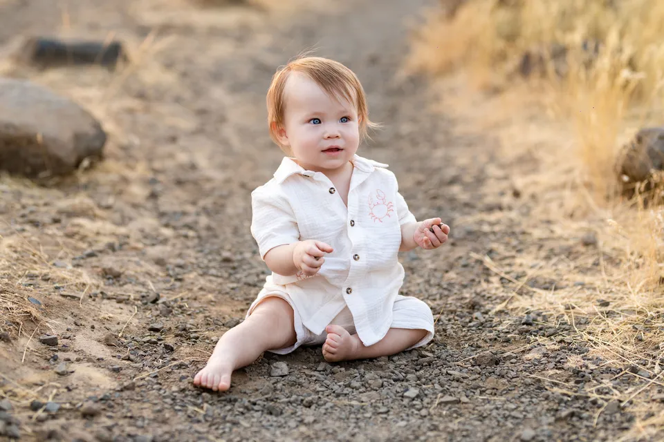 A baby sitting on a path beside golden summer grasses