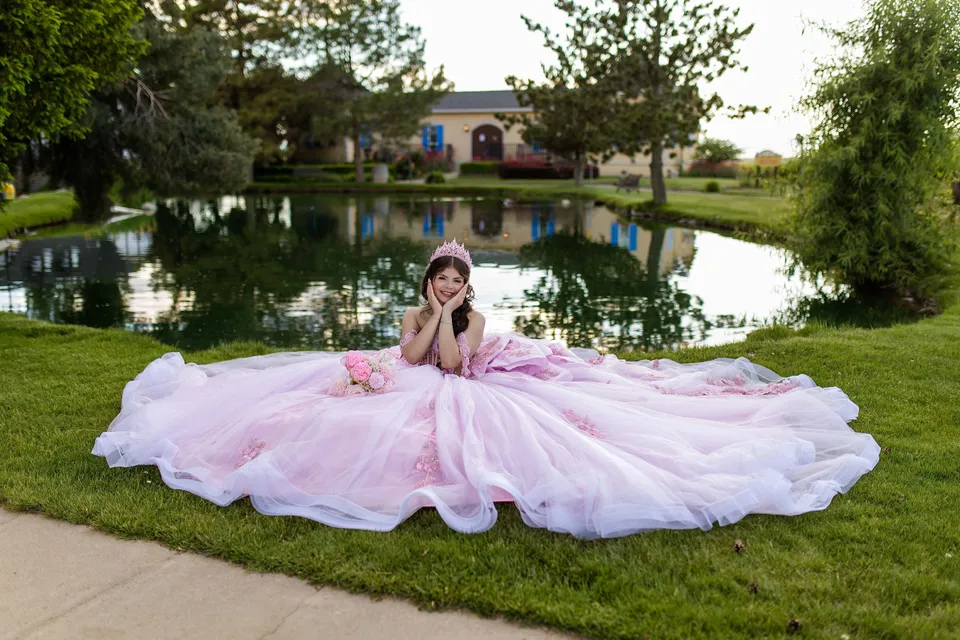A quinceañera in a pink gown seated beside a garden pond