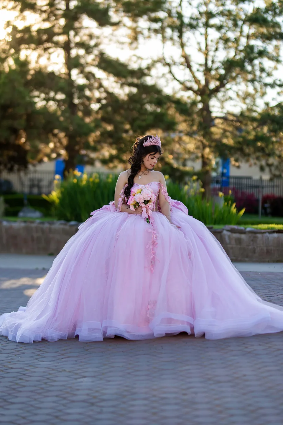 A pink quinceañera gown and bouquet in a sunlit garden