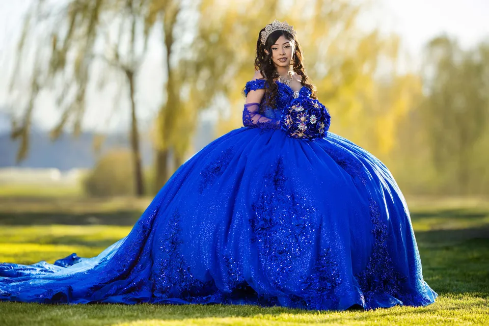 A quinceañera in a blue gown beneath garden willow branches