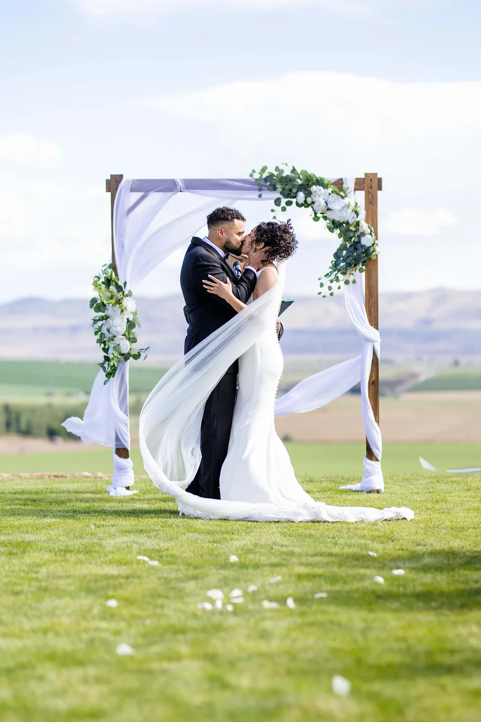 A wedding kiss beneath an outdoor floral ceremony arch