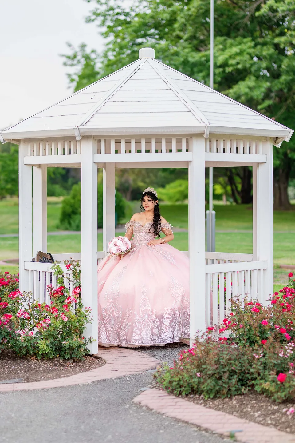 Retrato de quinceañera con vestido rosa en un quiosco blanco de jardín